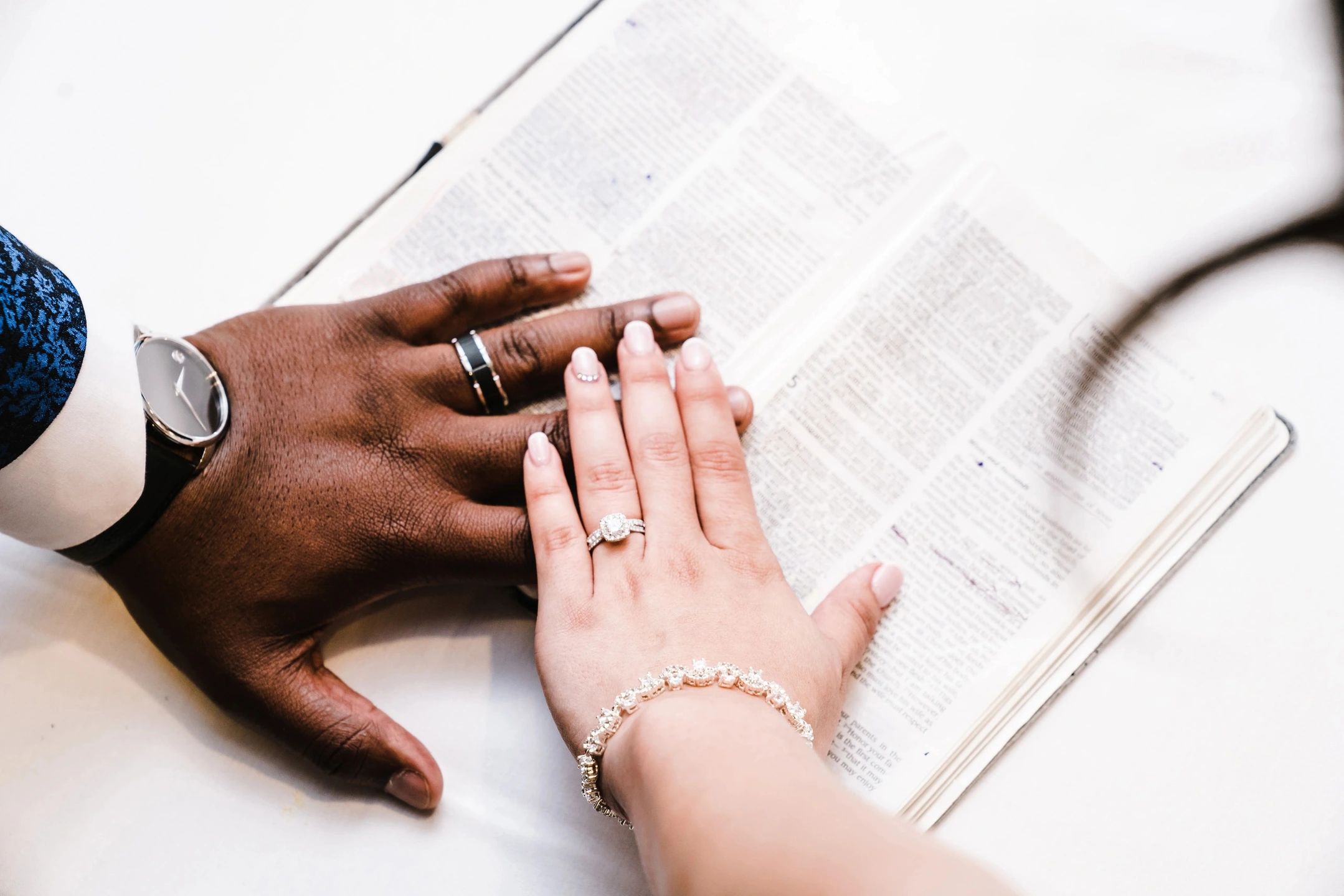 Two hands with wedding rings on, resting on a book.