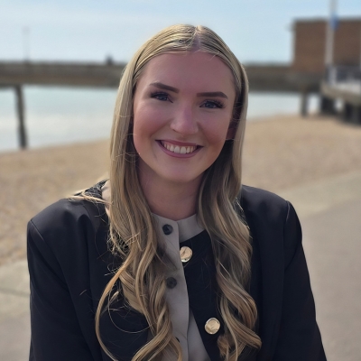 a picture of Nicole Dunn sat on Deal Seafront with the pier in the background.